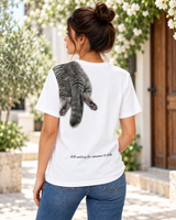Back view of woman wearing a white VZAEMOA graphic tee with grey shoulder cat artwork outdoors