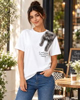 Woman wearing a white VZAEMOA graphic tee with grey shoulder cat artwork in a cafe setting